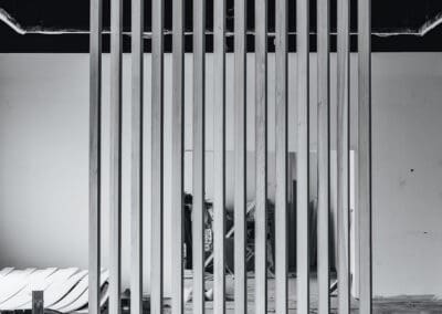 Black and white photo of a modern wooden slatted room divider standing in an unfinished industrial space, with exposed ceilings and a concrete floor.