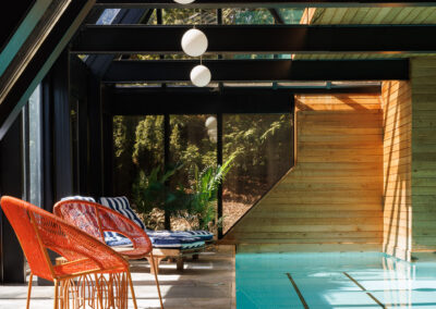 Modern indoor swimming pool with orange chairs, wood accents, large windows, and natural light.