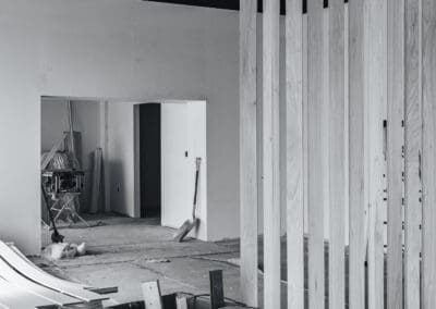 Black and white photo of an interior commercial space under construction, featuring a wood slat room divider, exposed ceiling, and building materials.