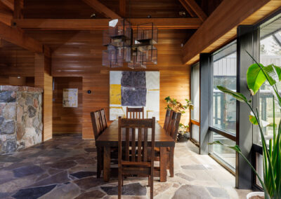 Rustic modern dining room with wood paneled walls, flagstone floor, dark wood table, and geometric chandelier under exposed beams.