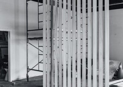 Black and white image of a wooden slatted room divider or partition in an unfinished interior space with scaffolding.