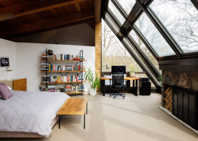 Modern bedroom and home office with large angular windows, stone fireplace, and wood vaulted ceiling.