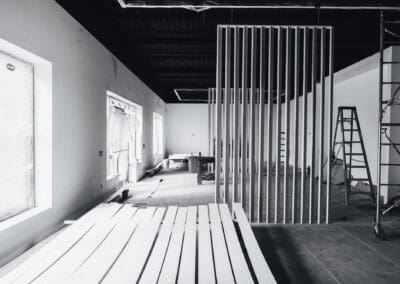Black and white interior shot of a commercial space under renovation with a slatted room divider, construction materials, and scaffolding