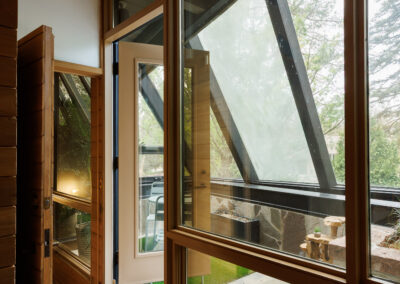 Modern home interior with large wood-framed windows and glass door leading to a stone patio, showcasing contemporary architectural design.