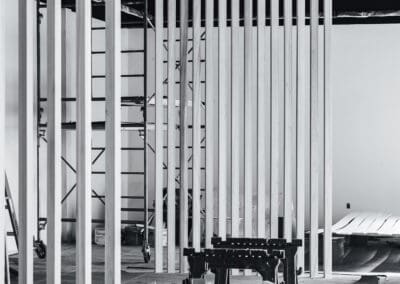 Black and white image of an interior commercial space under construction, featuring vertical wooden slat dividers, scaffolding, sawhorses, and building materials.