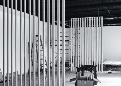 Black and white photo of an interior commercial space under construction with vertical slat dividers, scaffolding, and building materials.