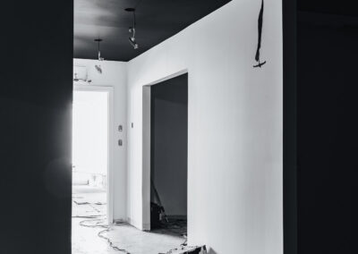 Black and white image of an interior space under renovation with freshly painted black ceilings and white walls, drop cloths, and Dulux paint cans.