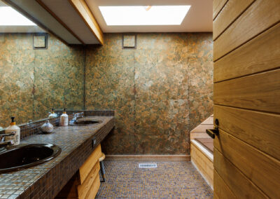 Modern bathroom with dual sinks, mosaic tile vanity, leaf pattern wallpaper, wood accents, and a skylight.