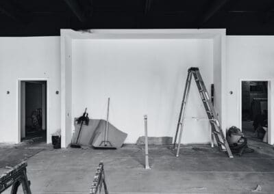 Black and white photo of an unfinished commercial interior space under renovation, featuring a ladder and construction tools.