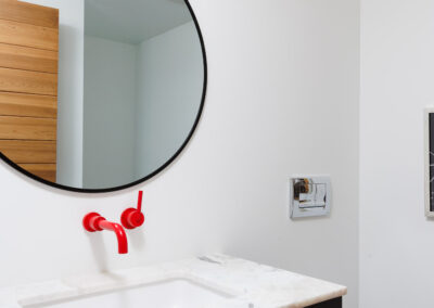 Modern bathroom with a round mirror, red wall-mounted faucet, marble countertop, and black floating vanity.