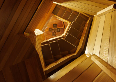 Overhead view of a warm wooden spiral staircase with carpeted steps and a unique square ceiling light fixture at the bottom.
