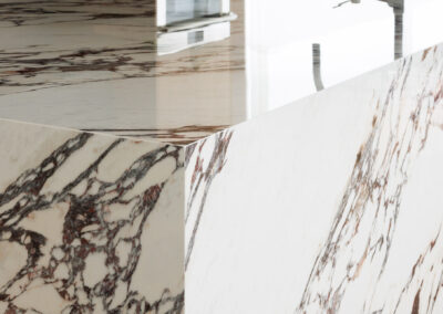 White marble surface with polished finish and distinct dark brown and reddish-brown veining, reflecting light.