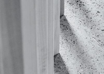 Abstract black and white image of vertical wooden slats casting long shadows on a speckled terrazzo floor.