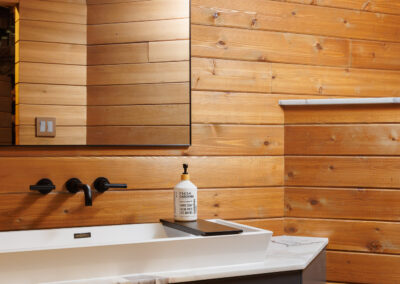 Modern bathroom with warm horizontal wood paneling, a white floating vanity, black wall-mounted faucet, and large mirror.