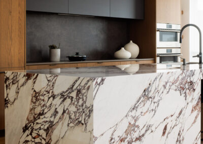 Modern kitchen with a striking purple-veined white marble island, light wood cabinetry, and dark gray accent cabinets.