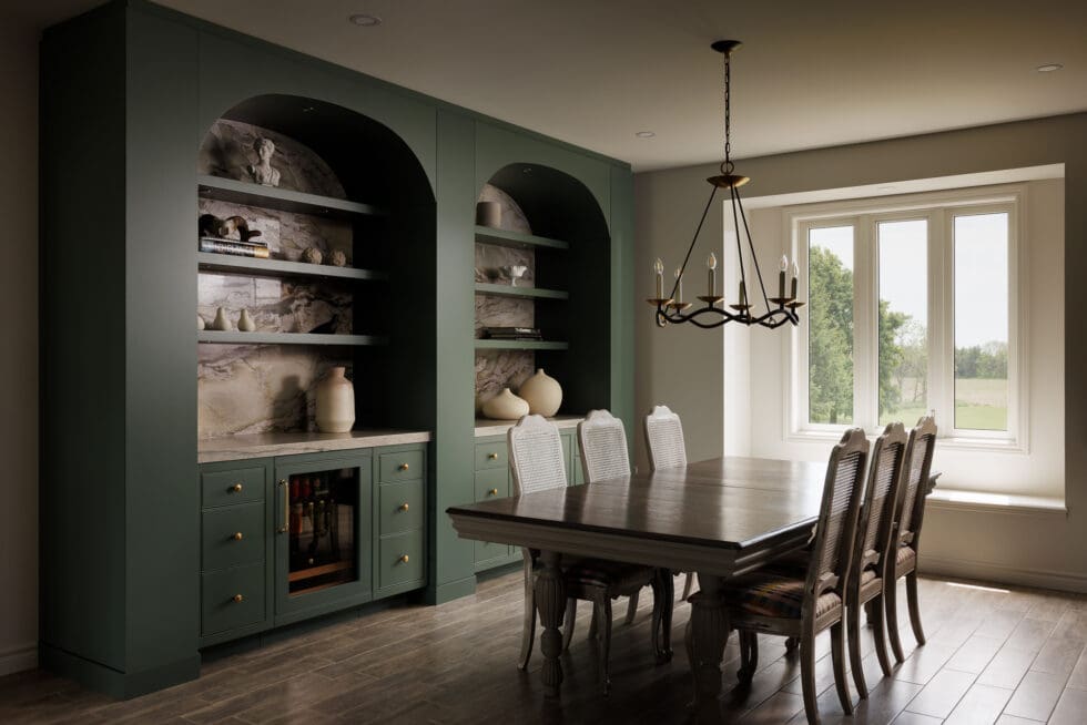 Elegant dining room with custom dark green built-in cabinets, marble-backed shelves, an integrated wine fridge, a large wooden dining table with cane-back chairs, and a chandelier, all illuminated by a bright window overlooking a natural landscape.