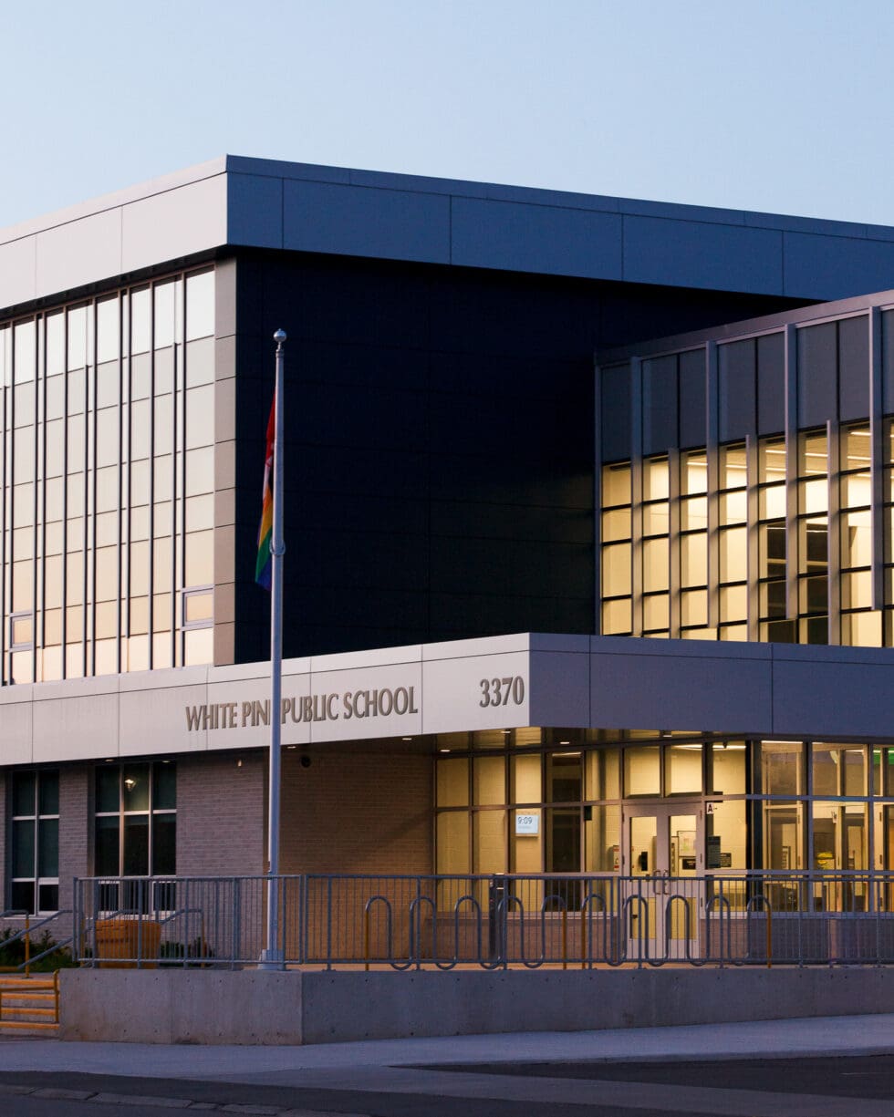 White Pine Public School building exterior with an Indigenous flag, modern architecture, and glowing windows.