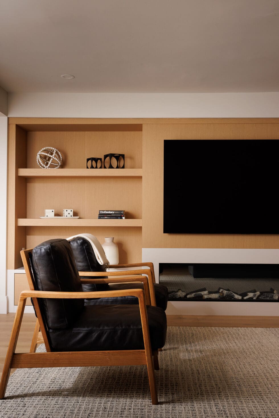 Modern living room with black leather armchairs, wood shelving, flat-screen TV, and electric fireplace
