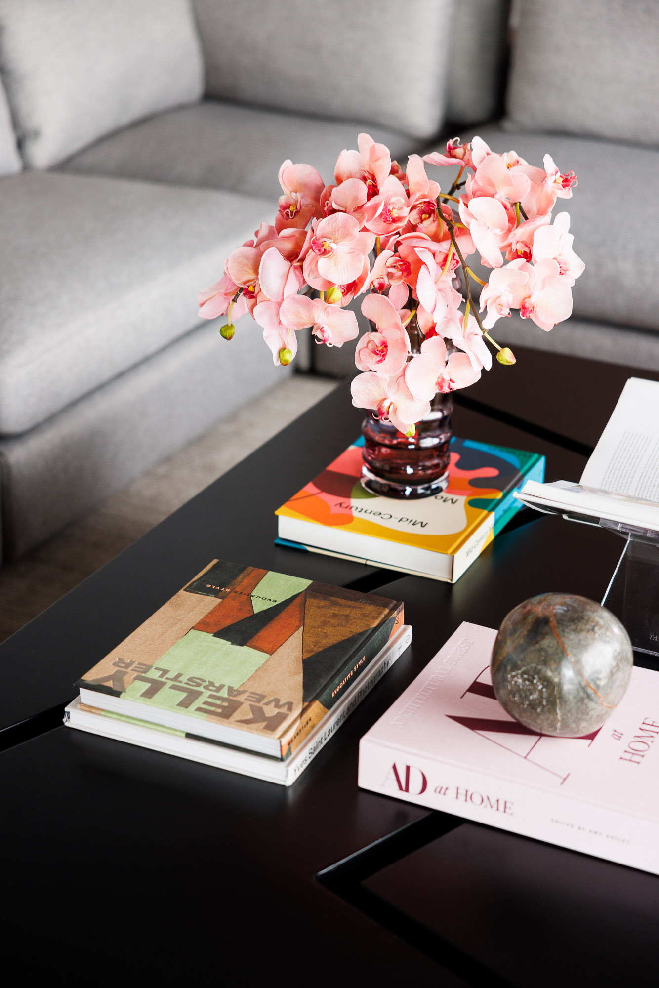 High-End Coffee Table Styling Overhead shot of a black coffee table styled with Kelly Wearstler books, pink orchids, and a polished stone sphere.