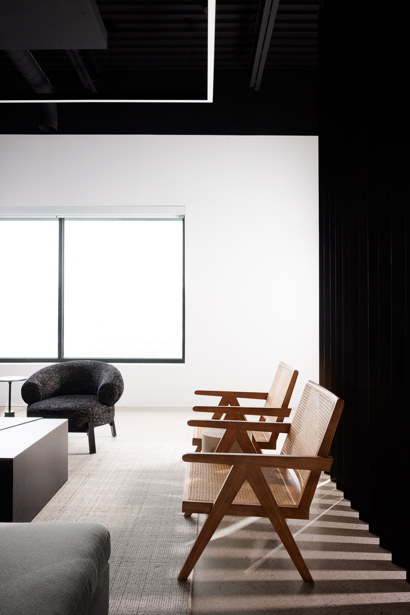 Interior view of a bright lounge area with Pierre Jeanneret style chairs and an open black industrial ceiling.