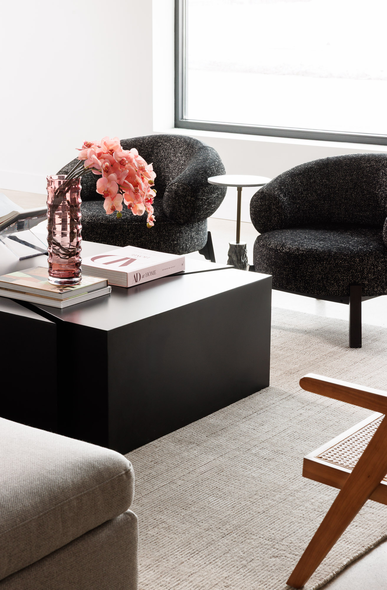 Detailed view of two textured black rounded armchairs next to a minimalist coffee table with pink orchids.